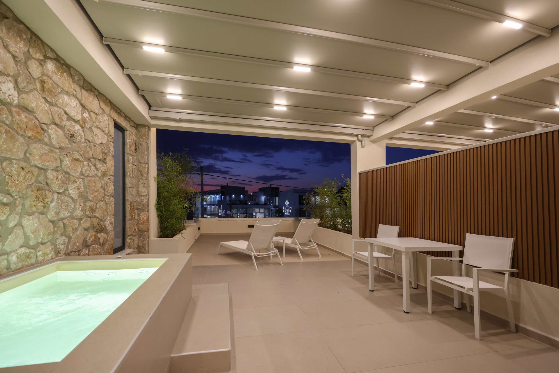 Furnished balcony terrace with sun loungers, dining table and Jacuzzi at night